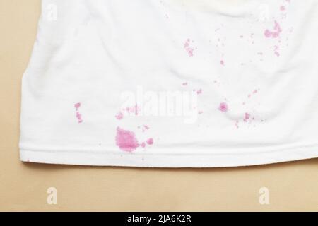 dirty stains on a white T-shirt from berries and drink on beige background. Stock Photo