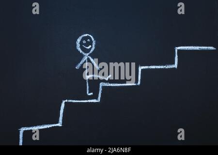 the drawn man on the chalk board climbs up step by step to the top of career stairs. copy space Stock Photo