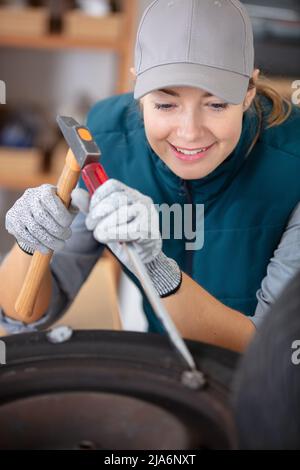 female mechanic using a hammer while working on a tyre Stock Photo
