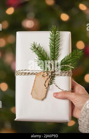 Unrecognizable womans hand holding gift box prepared and decorated for Christmas boxing day, vertical close-up shot Stock Photo