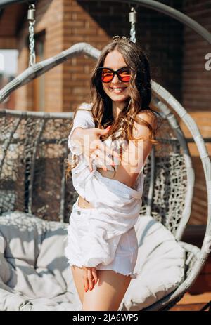 Bachelorette party. Happy future bride in a white shirt and shorts poses on the roof of the house overlooking the city. Stock Photo