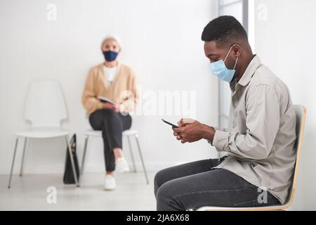 Horizontal shot of unrecognizable African American man and senior woman wearing masks waiting for medical consultation Stock Photo