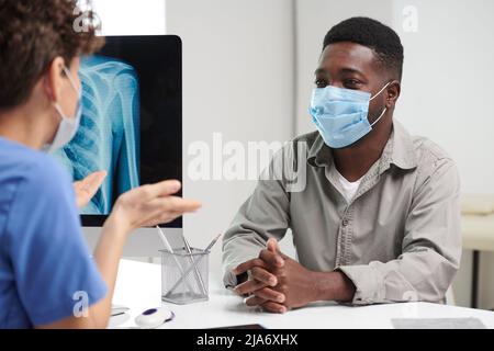 Over-the-shoulder shot of unrecognizable African American man wearing protective mask on face having medical consultation Stock Photo