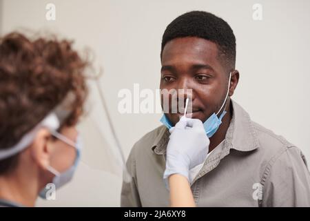 High angle medium close-up shot of unrecognizable doctor wearing protective masks testing African American male patient for viral disease Stock Photo