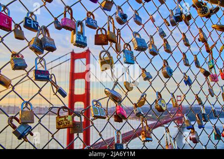 Chain link fence covered in locks with hole revealing Golden Gate Bridge in background Stock Photo