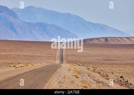 Desert road going through empty hills and plains leading to mountains Stock Photo