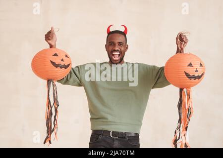 Portrait of emotional excited young Black man with beard holding Halloween paper lanterns against isolated background Stock Photo