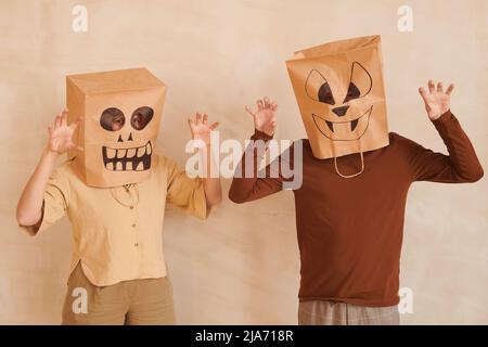 Young couple in funny paper bag masks making scaring gestures against beige background on Halloween Stock Photo