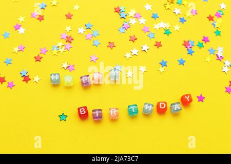 inscription happy birthday and multicolored confetti in the form of stars on a yellow background Stock Photo