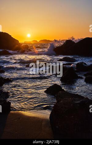 California beaches with ocean waves crashing over rocks during sunset Stock Photo