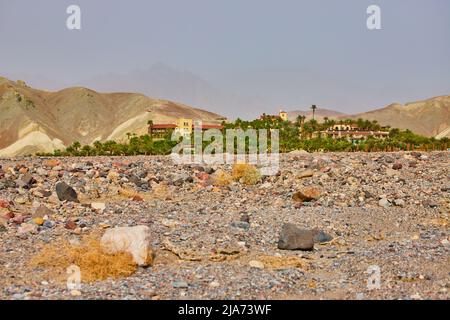 Hotel oasis filled with palm trees fully surrounded by sandy desert plains and mountains Stock Photo