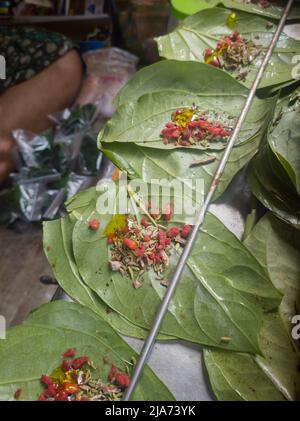 Betel leaves or mitha paan being prepared with ingredients like areka nut or supari and other condiments in a shop for sale in india. A famous practic Stock Photo