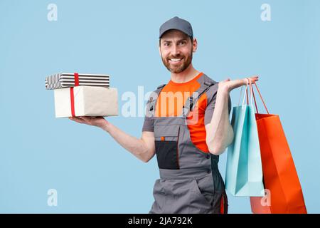 Delivery man in uniform holding shopping bags and gift boxes on blue studio background Stock Photo
