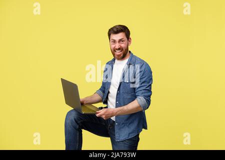 Crazy smiling man with beard holding laptop on leg and looking at camera. Studio shoot Stock Photo