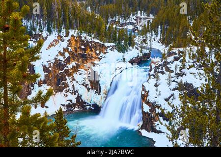 Amazing blue and peaceful waterfall by snowy cliffs and pine trees in Yellowstone Stock Photo