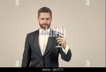 handsome tuxedo man cheers with glass of red wine hold gift box behind back, copy space, sommelier Stock Photo