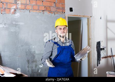 Builder in the helmet ready is plastering the wall Stock Photo