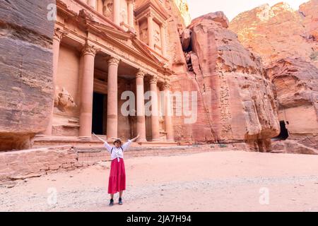 Rear view of beautiful young woman standing with open arms  in front of the treasure of petra, Jordan Stock Photo