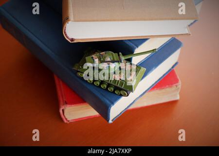 camouflage toy tank stacked on old war books on brown wooden table Stock Photo