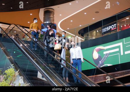 Budapest, Hungary - November 20, 2021: young people in face masks due to coronavirus danger restrictions go down the escalator in a big shopping mall Stock Photo