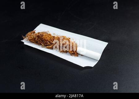 Rolling tobacco with filter tip and paper, isolated on black background Stock Photo