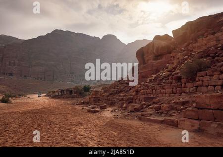 Typical landscape at Petra, Jordan, red dusty ground, mountains with carved buildings inside in distance Stock Photo