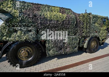 Armoured truck completely covered with camouflage mesh net parked at pavement on sunny day, side view Stock Photo