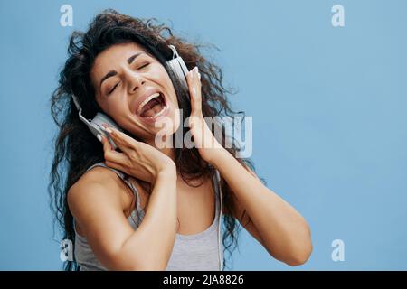 MUSIC STREAMING PLATFORM AD CONCEPT. Enjoyed beautiful curly female in headphones, listen favorite playlist, sing, dance. Studio shoot isolated with Stock Photo