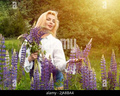 Woman walks in the garden full of lupines Stock Photo