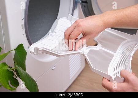 A man takes a lint filter out of the dryer and cleans it from dust, lint, hair, wool. Stock Photo