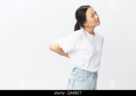 Back pain. Suffering from osteochondrosis after long study pretty young Asian woman touching painful lower back posing isolated on white background Stock Photo
