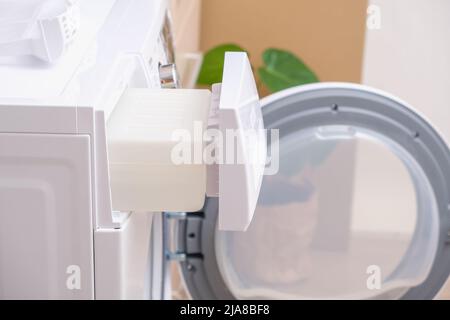 A man takes out a container from the dryer to collect water squeezed out of wet laundry. Stock Photo
