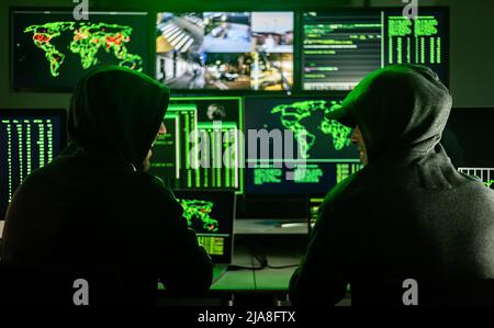 Two male hackers coding virus software in dark room Stock Photo