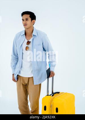 Ready to trip. Passport with flight ticket in young Asian man's hand while walking and holding yellow suitcase handle isolated on white background, ve Stock Photo