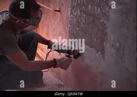 A man using a grinder to remove wallpaper in the apartment Stock Photo
