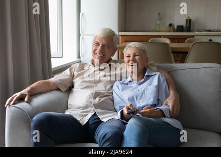 Laughing elderly spouses cuddle on couch watch tv movie comedy Stock Photo