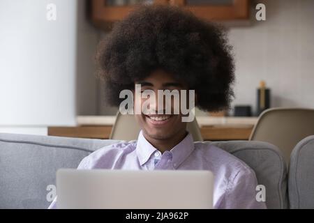 Happy cheerful Black student guy using laptop on sofa Stock Photo