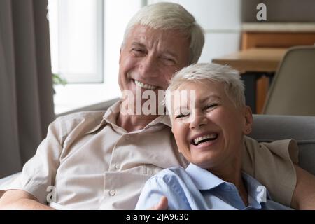 Laughing older couple embrace on sofa having fun at home Stock Photo