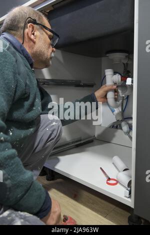 Mature plumber installing sink siphon in domestic kitchen. Stock Photo