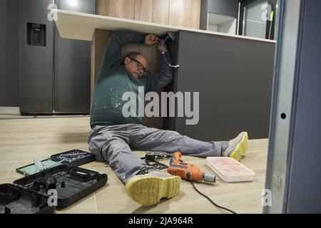 Mature man installing corner socket with screwdriver sitting on floor. Stock Photo