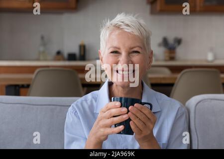 Happy senior grandmother look at camera hold cup of tea Stock Photo