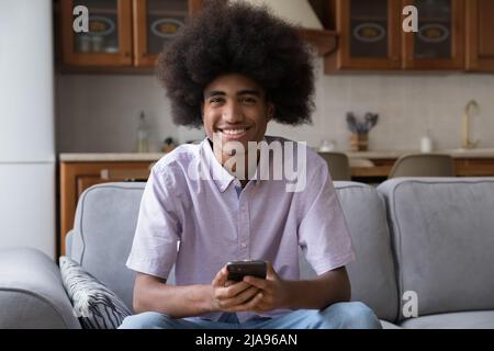 Happy guy with long fuzzy curly hair using smartphone Stock Photo
