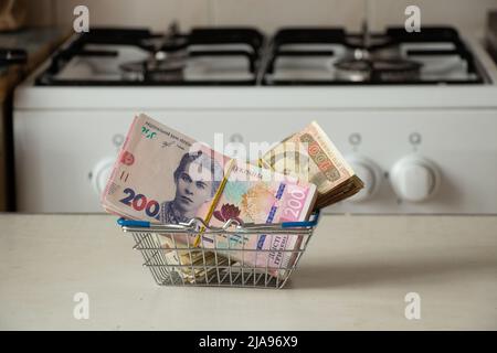 One hundred and two hundred hryvnias in a basket from a supermarket lie on a table near a gas stove in the kitchen, Ukrainian hryvnia and gas, finance Stock Photo
