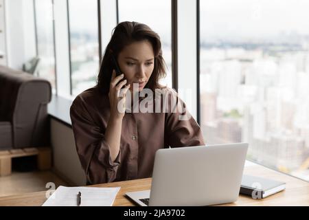 Serious businesswoman talking on mobile phone at office workplace Stock Photo