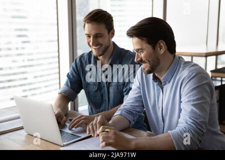 Happy startup partners using laptop and discussing project at workplace Stock Photo