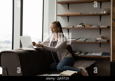 Focused adult student studying on couch with laptop and books Stock Photo