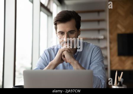 Thoughtful focused business man in glasses working at laptop computer Stock Photo