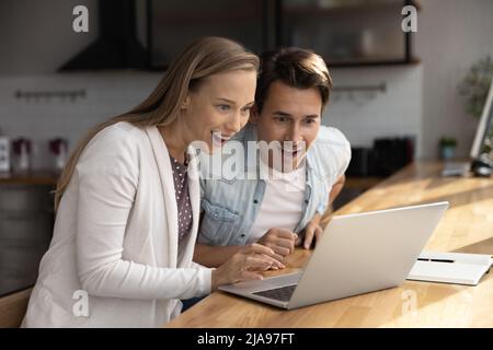 Happy surprised millennial couple using laptop, staring at screen Stock Photo