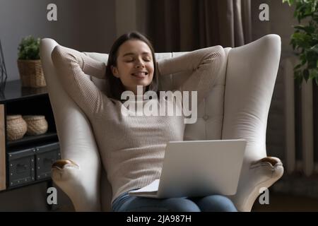 Dreamy cheerful millennial girl using laptop on lap Stock Photo