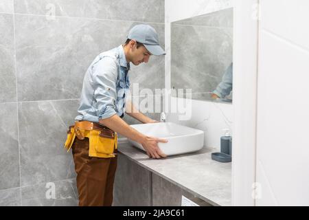 Professional plumber, male worker in uniform installing sink and water pipe in new apartment Stock Photo